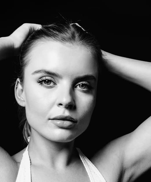 Black and white portrait of a woman with arms raised, highlighting toned upper arms and smooth skin