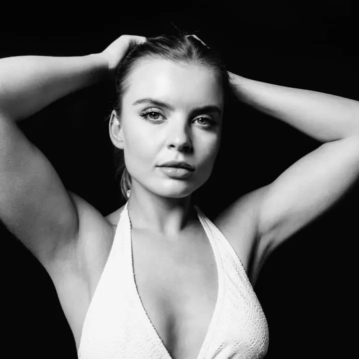 Black and white portrait of a woman with arms raised, highlighting toned upper arms and smooth skin