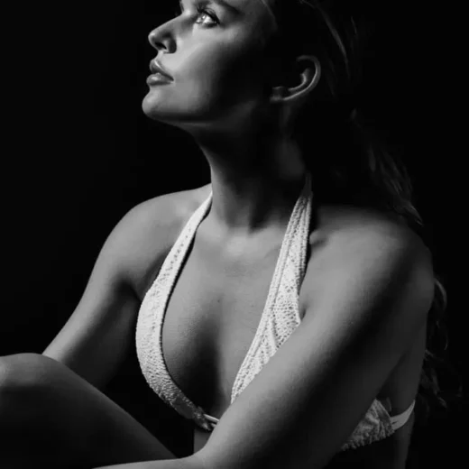 Black and white portrait of a woman in profile wearing a halter-style top, with soft lighting highlighting her jawline, neck, and upper body contours against a dark background.